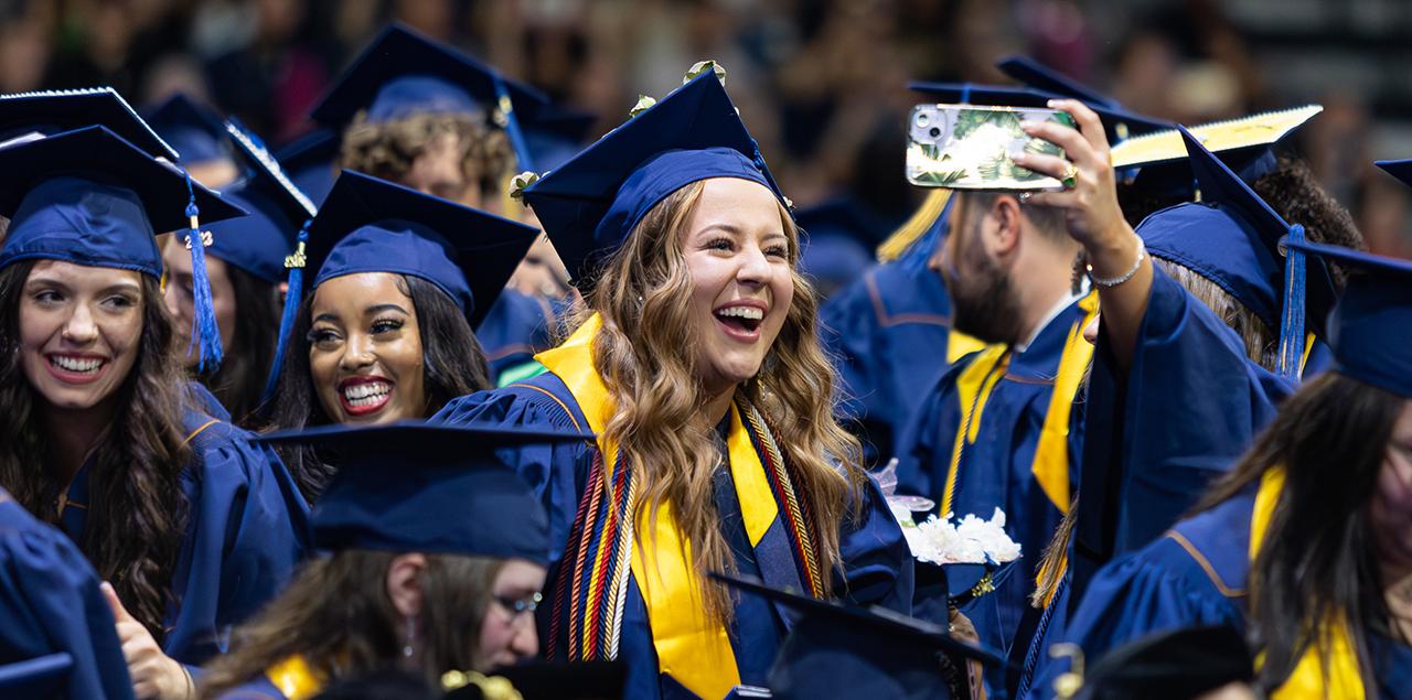 一群皇冠app官方版下载的学生在毕业典礼上戴着帽子，穿着长袍，微笑着站在那里自拍